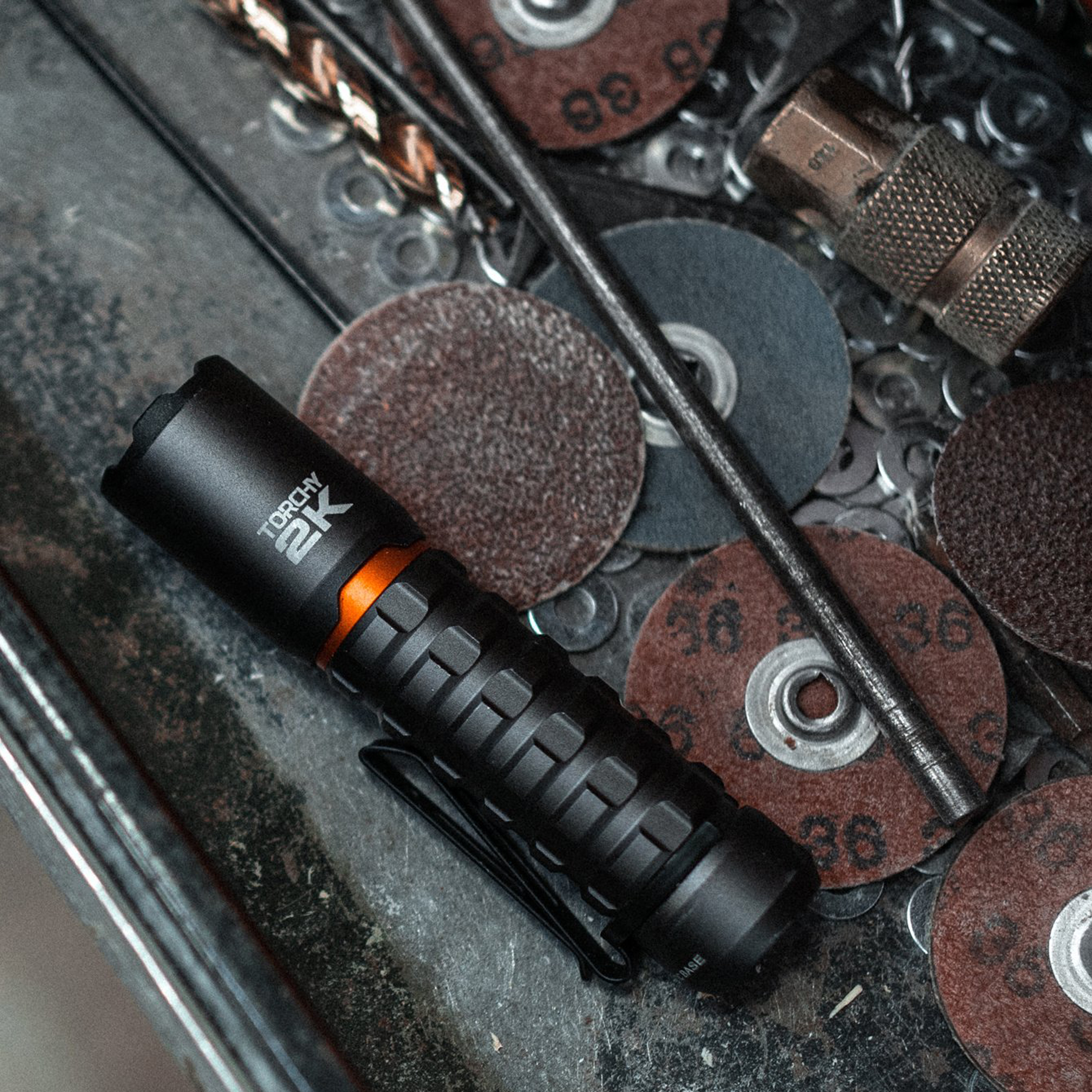 Lampe de poche noire avec accent orange, entourée d'outils et de disques abrasifs.