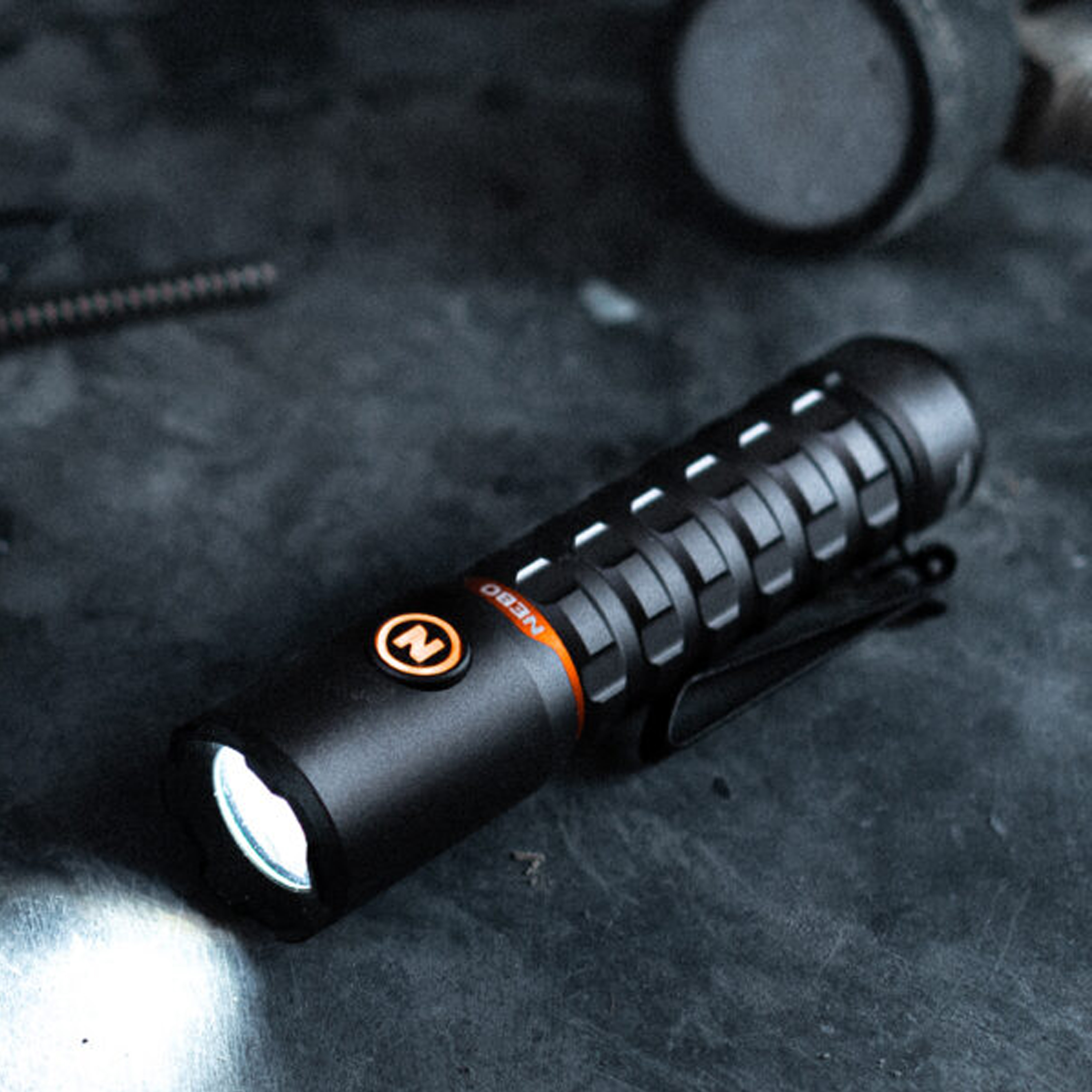 Une lampe de poche noire avec un anneau orange et l'inscription "Nebo" repose sur une surface sombre.
