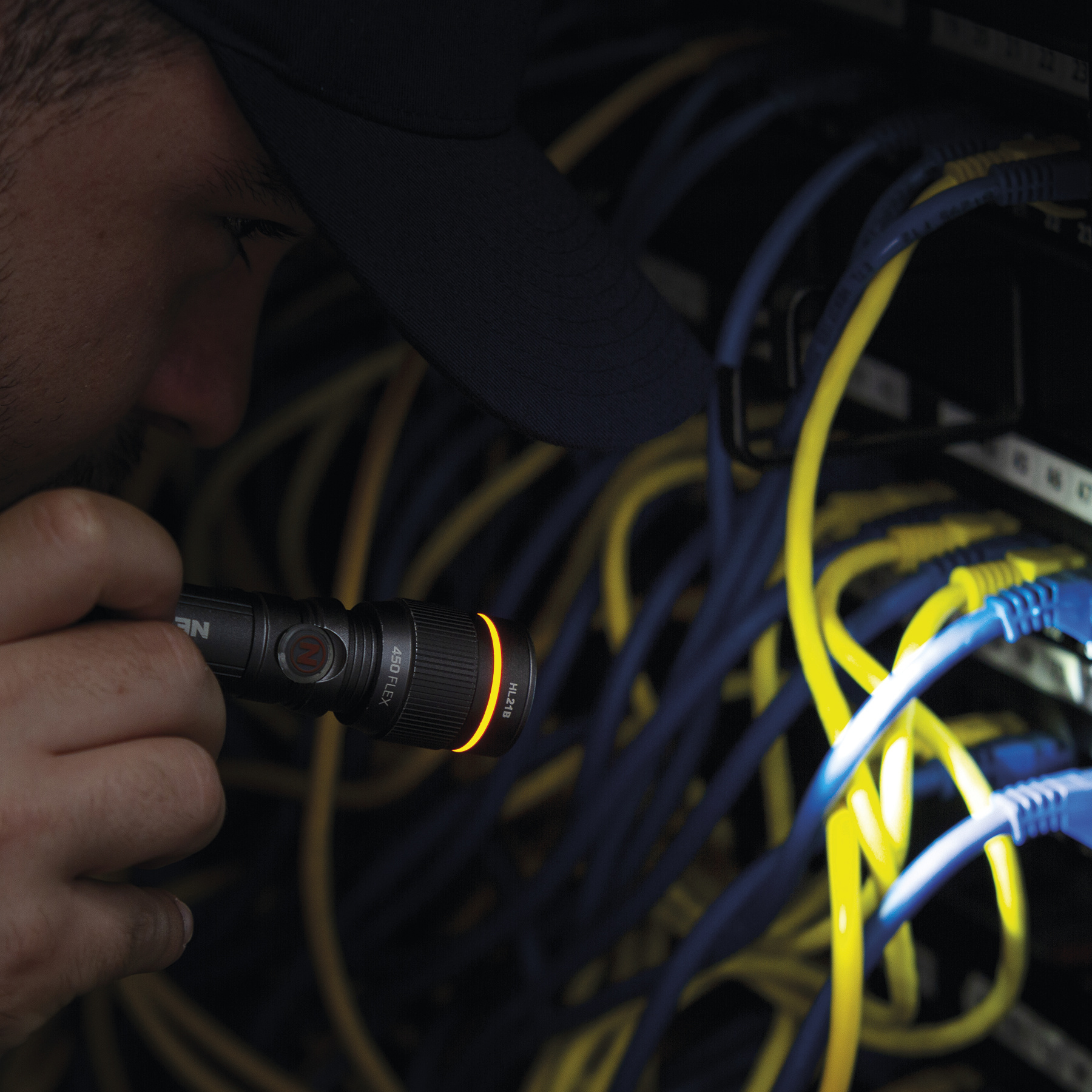 Mężczyzna oświetla latarką niebieskie i żółte kable w serwerowni.