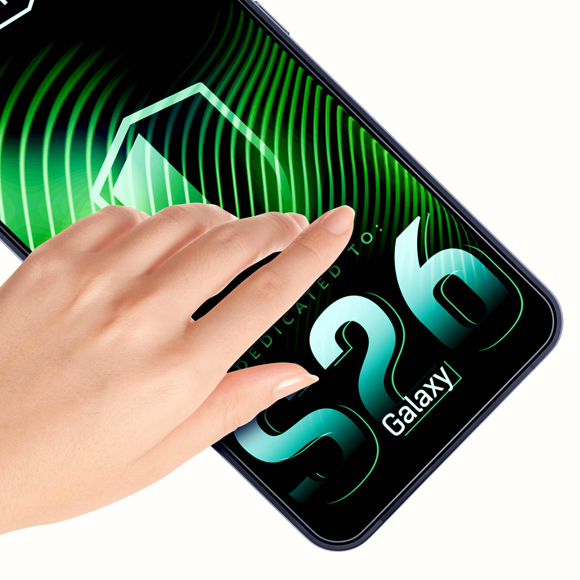 Una mano tocca un telefono Galaxy S26 con una grafica di sfondo verde ondulato.