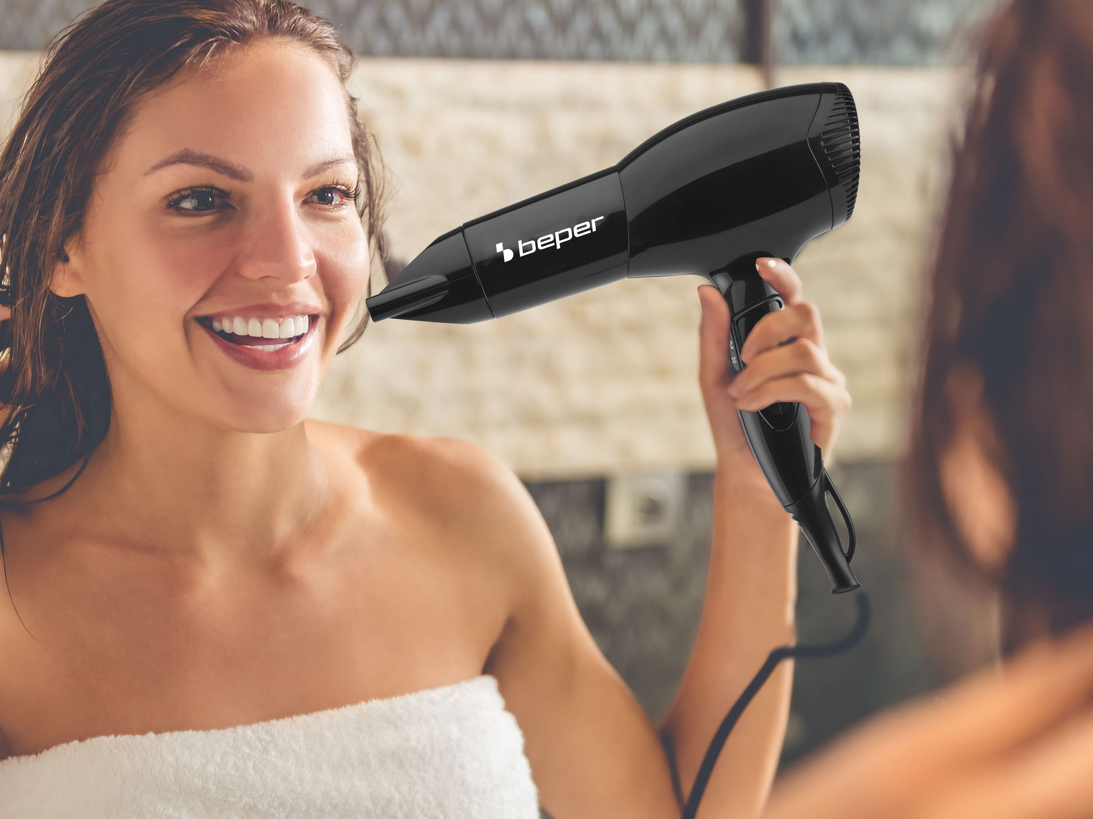 Donna asciuga i capelli con asciugacapelli nero, sorride allo specchio.
