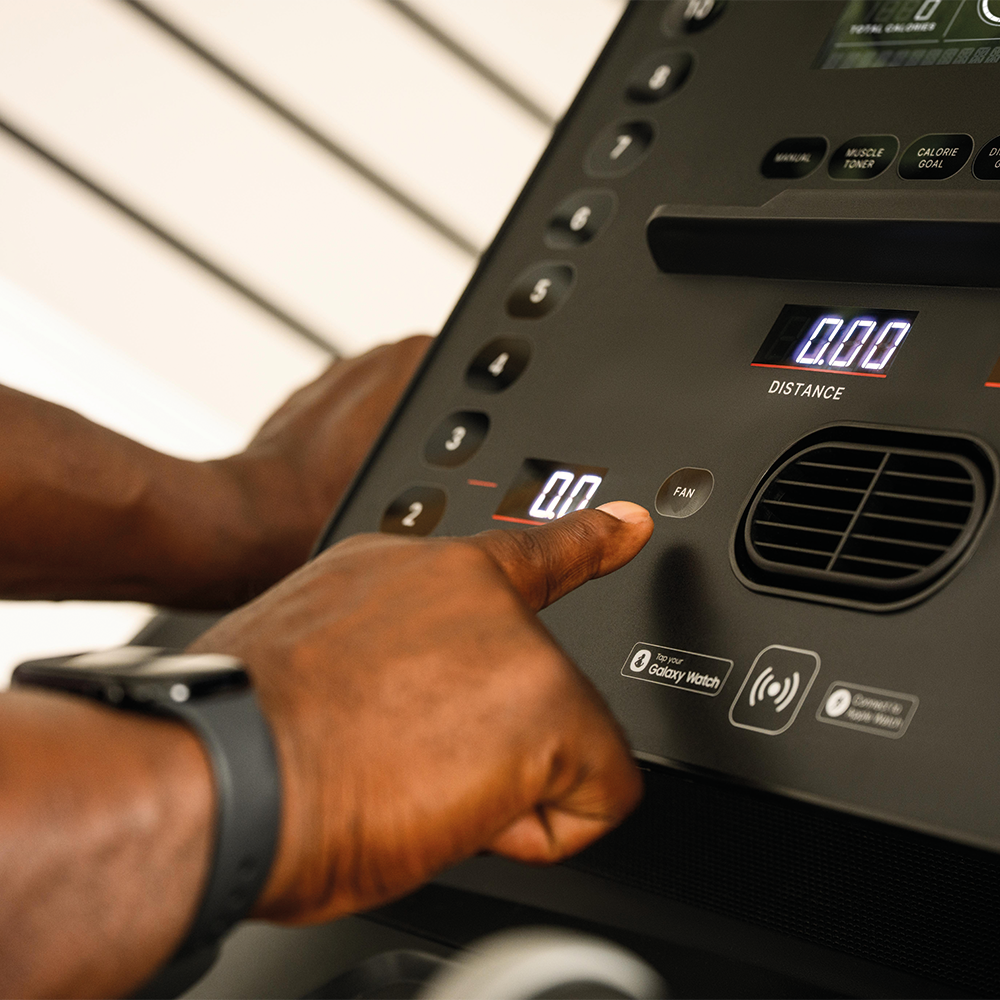 A man presses a button on a treadmill console. The display shows 0.00.