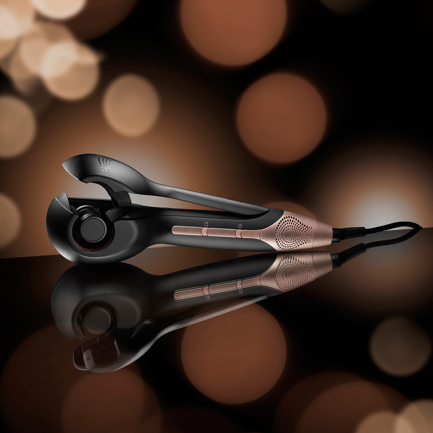 Czarna i różowo-złota lokówka odbijająca się na gładkiej powierzchni.