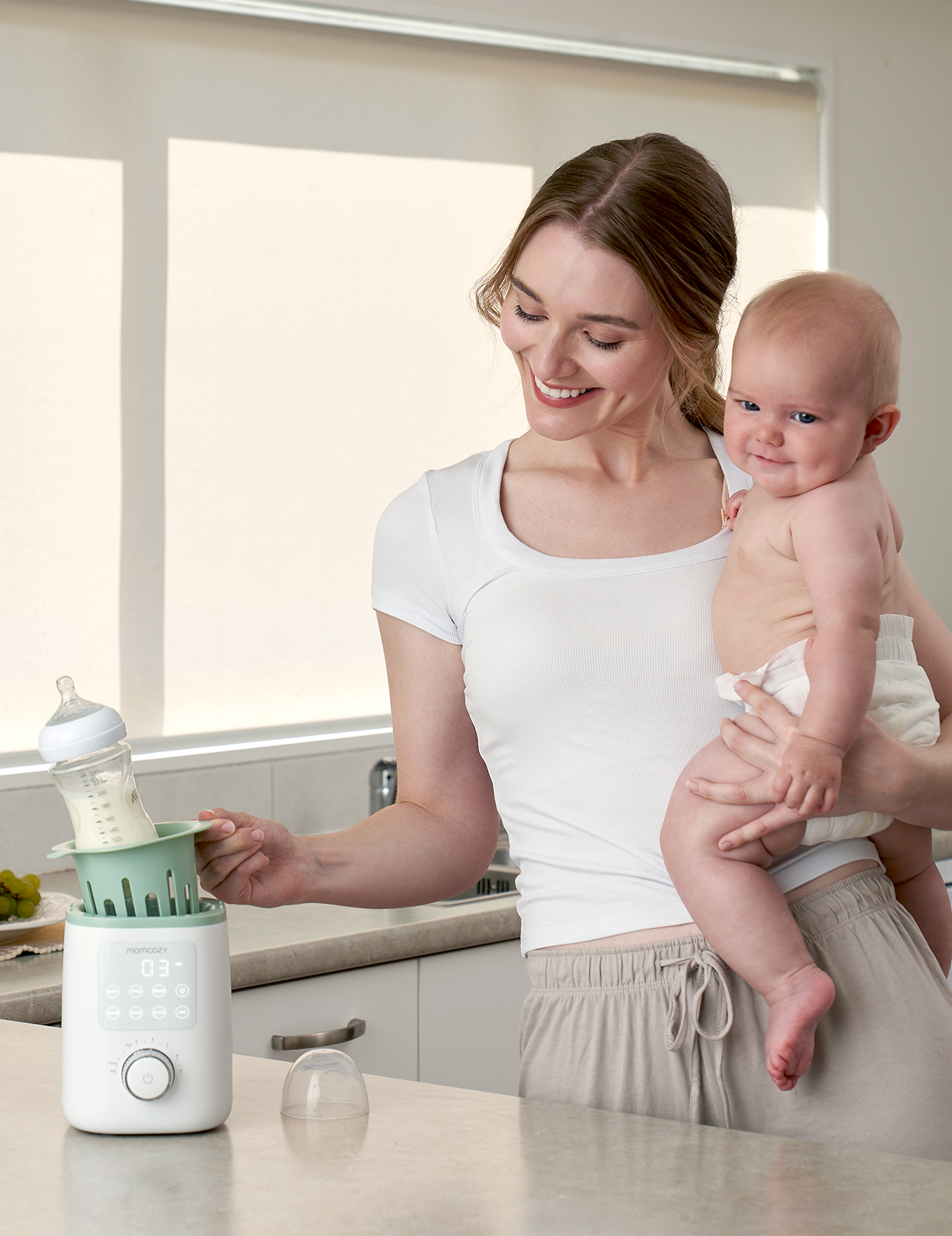 Frau hält Baby, benutzt Flaschenwärmer mit Babyflasche und Milch.