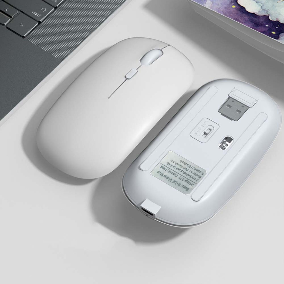 Due mouse wireless bianchi su una scrivania. Uno è capovolto, mostrando etichette e un ricevitore USB.