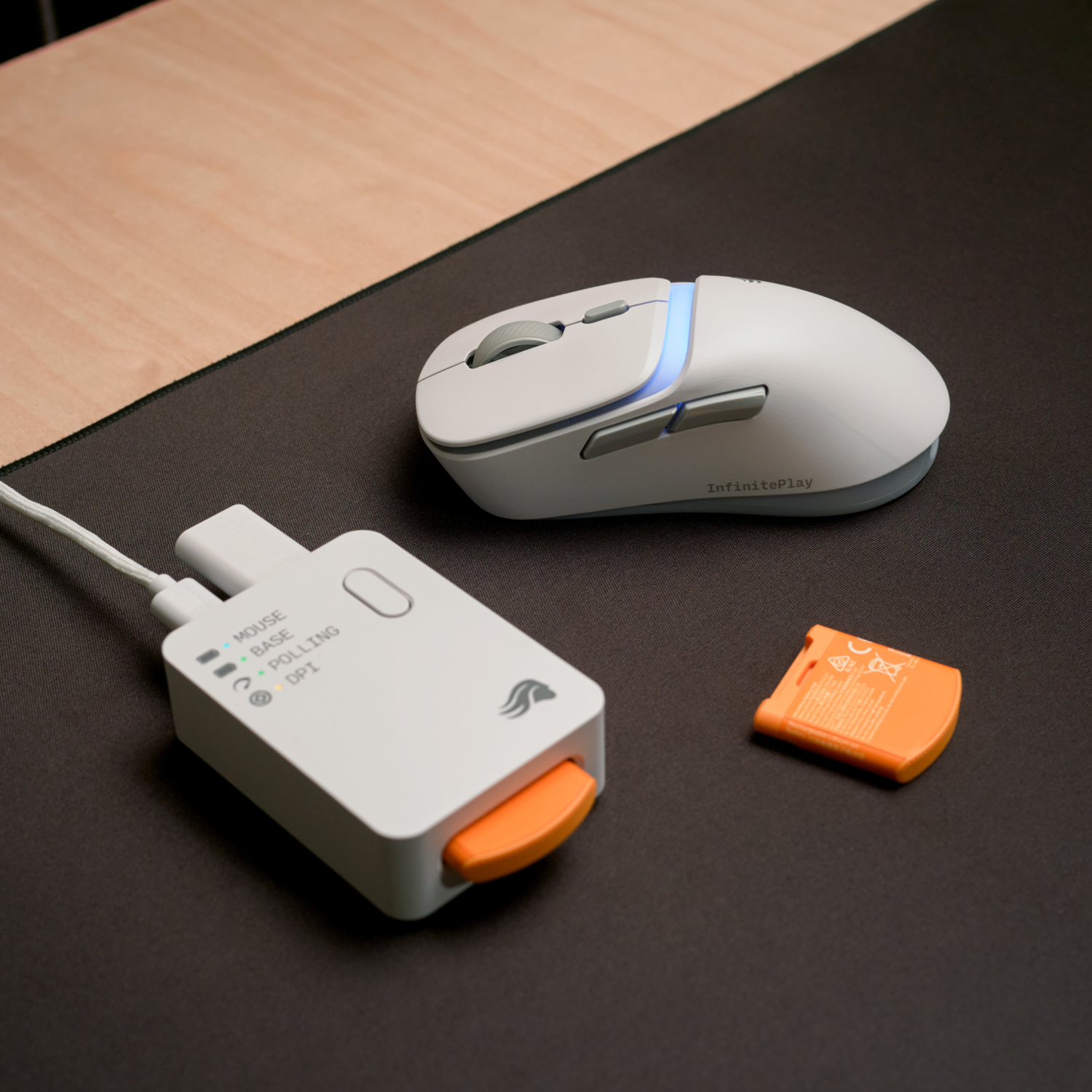 Mouse bianco, base di ricarica e batteria arancione su tappetino scuro.