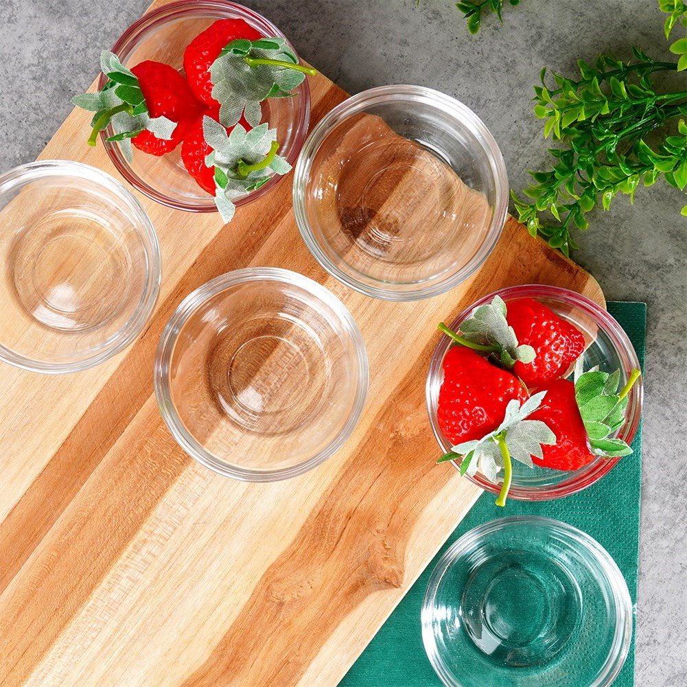 Cinco cuencos pequeños de cristal, dos con fresas y hojas, sobre una tabla de madera.