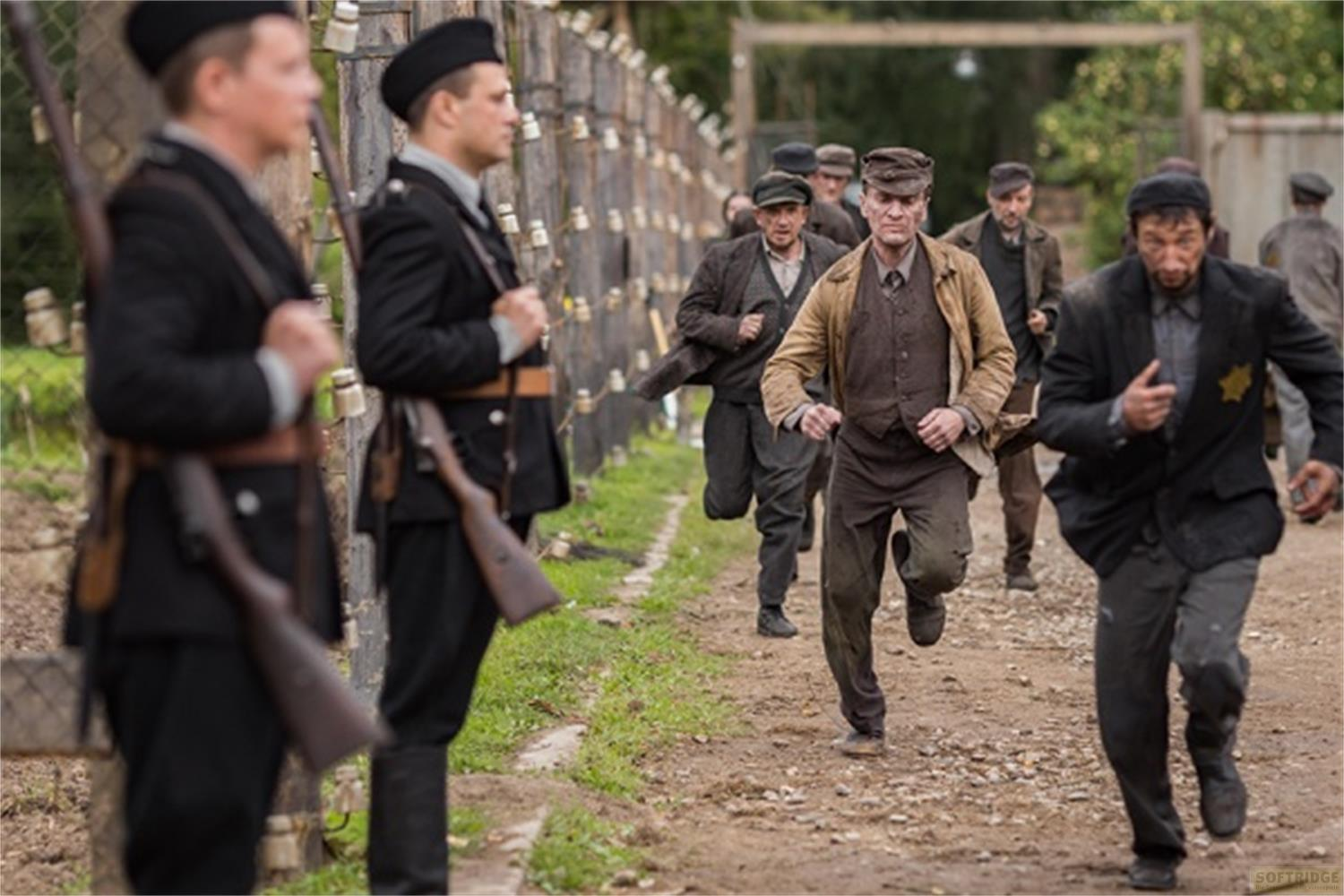 Des hommes en vêtements sombres courent sur un chemin de terre, gardés par des soldats.