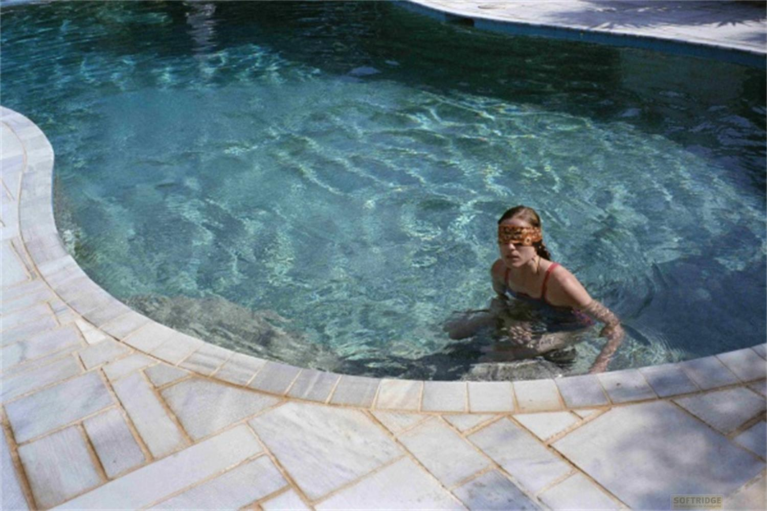 Una ragazza con una benda sugli occhi nuota in una piscina d'acqua limpida.
