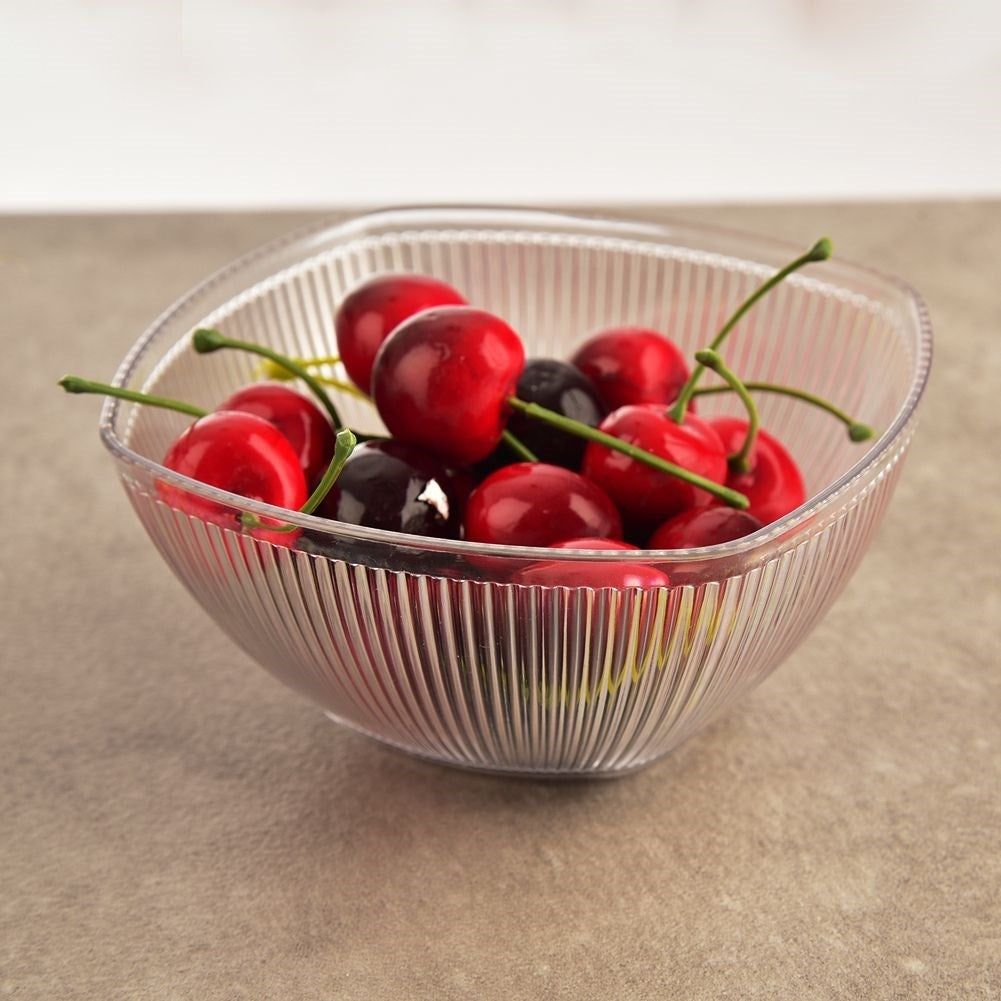 Cerezas rojas y oscuras en un cuenco transparente sobre una superficie de piedra.