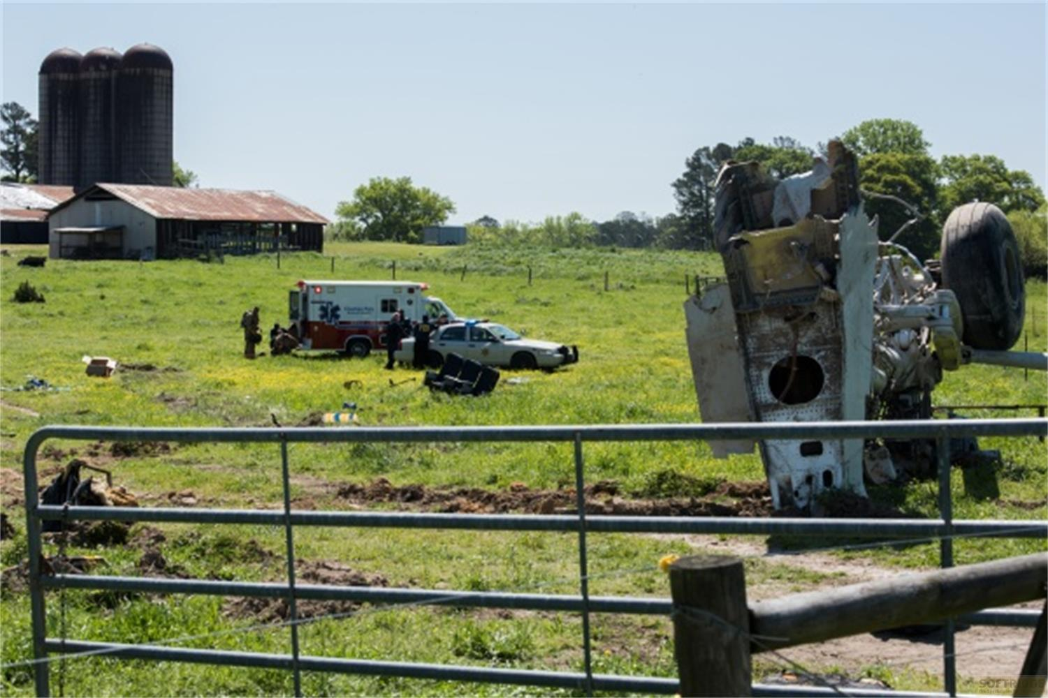 Detriti di aereo in un campo vicino a servizi di emergenza ed edifici agricoli.
