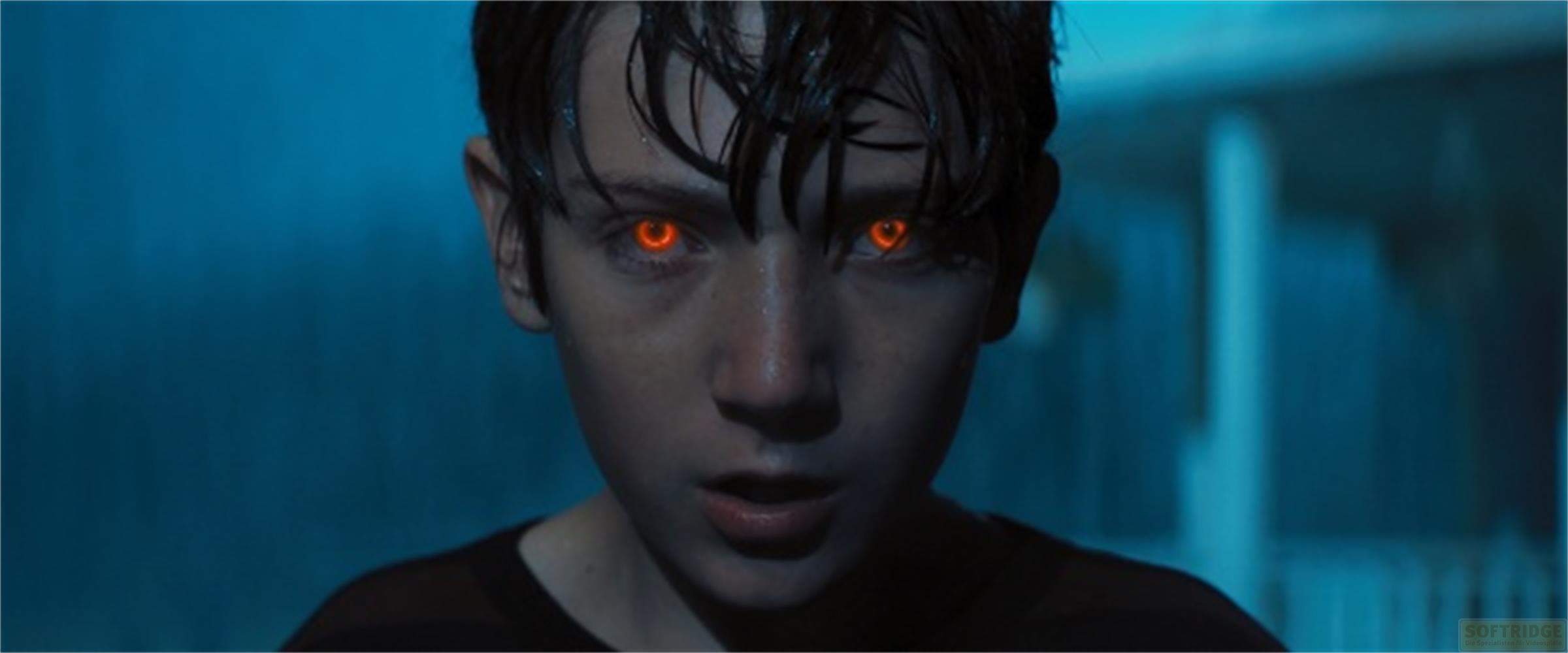 Un ragazzo con occhi arancioni luminosi guarda la telecamera. Luci blu.