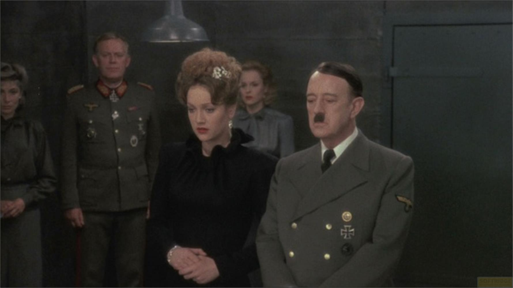 Ein Mann in Uniform und eine Frau in Schwarz stehen im Vordergrund, im Hintergrund stehen weitere Personen.