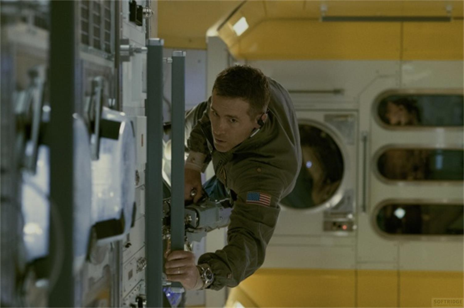 Astronauta in tuta verde con toppa bandiera americana fluttua in una stazione spaziale, aggrappandosi a una barra.