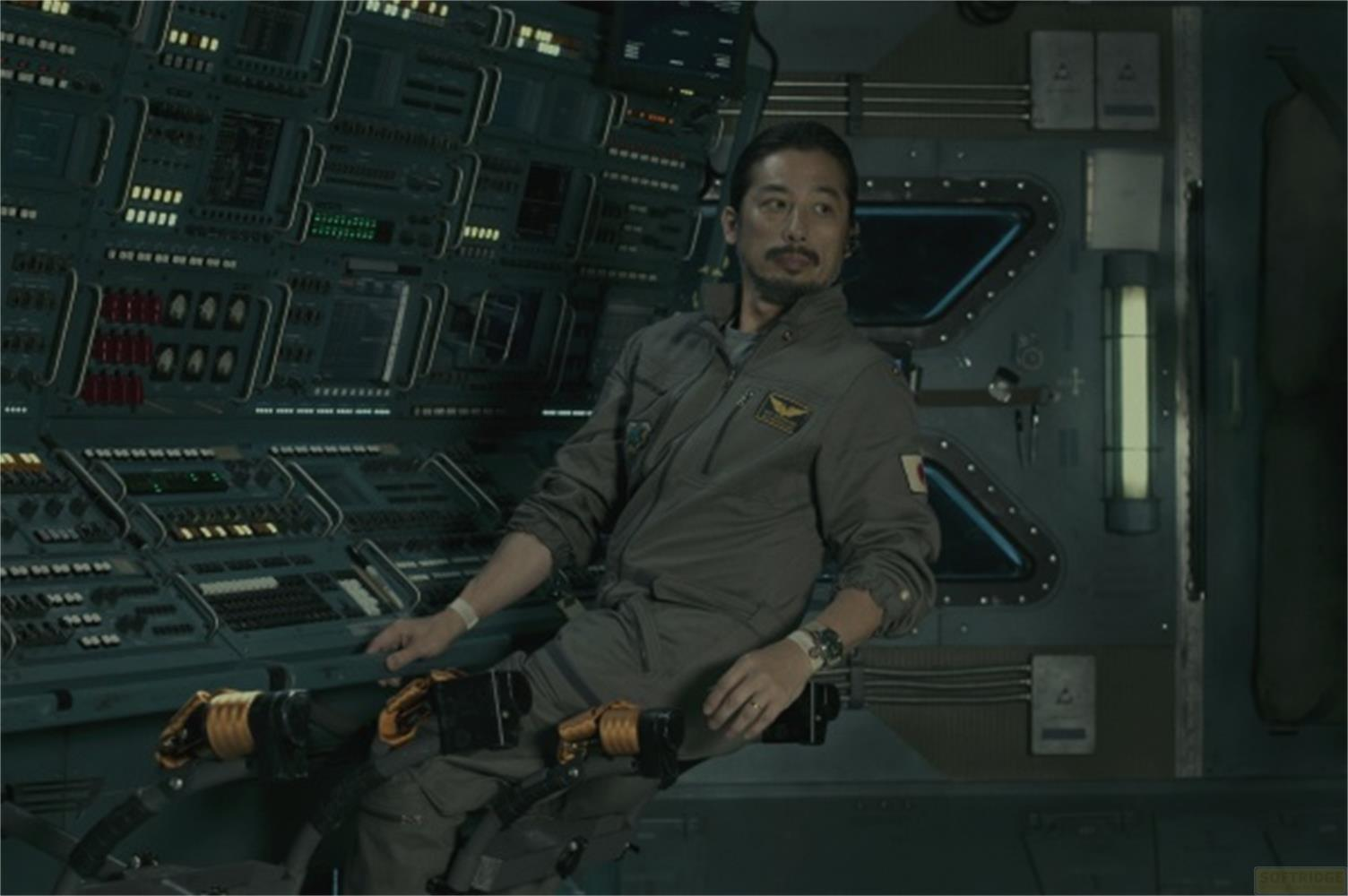 Un uomo in tuta spaziale grigia siede in una cabina con molti pulsanti.