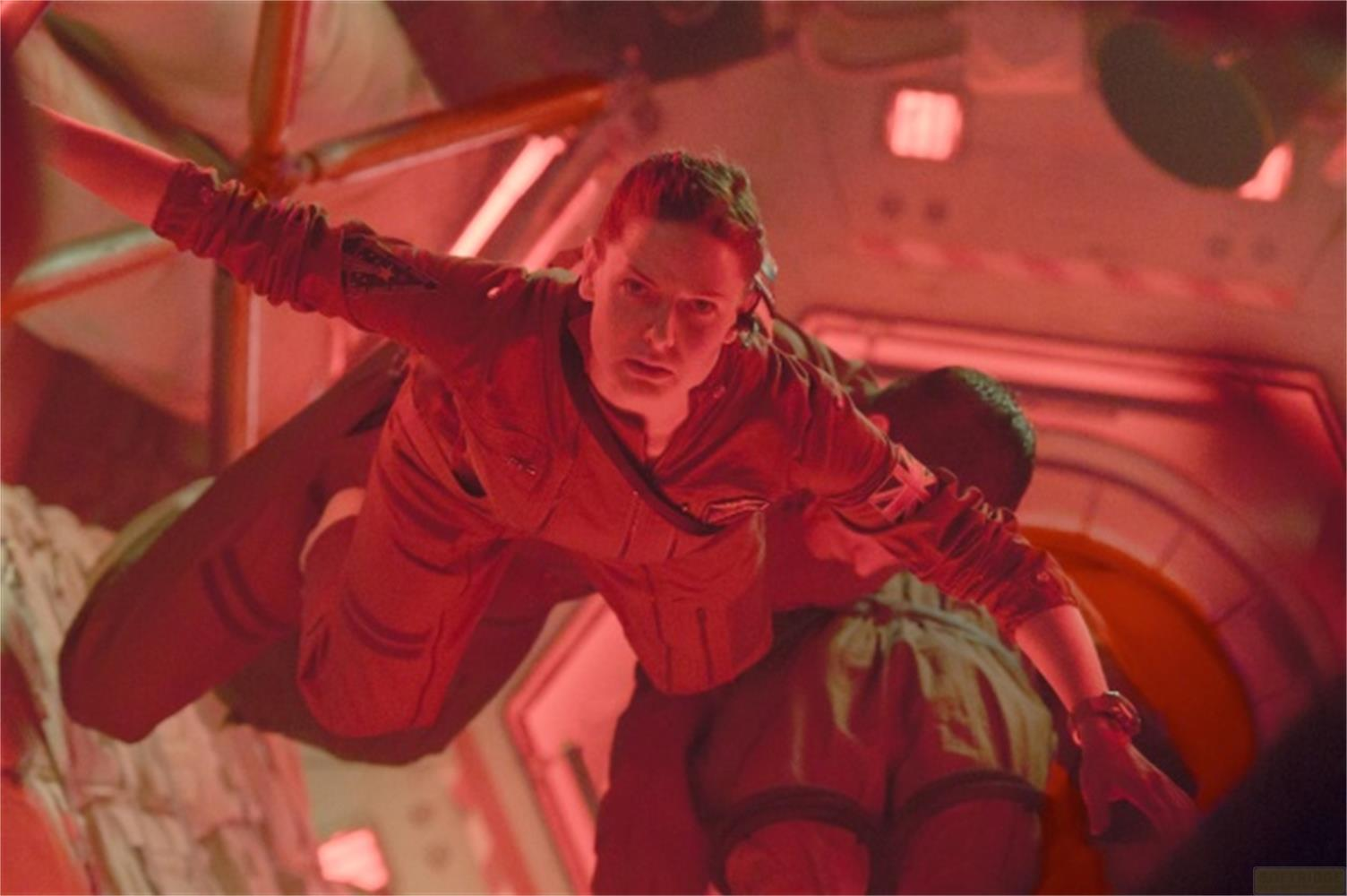Donna in tuta spaziale rossa fluttua in un'astronave illuminata.