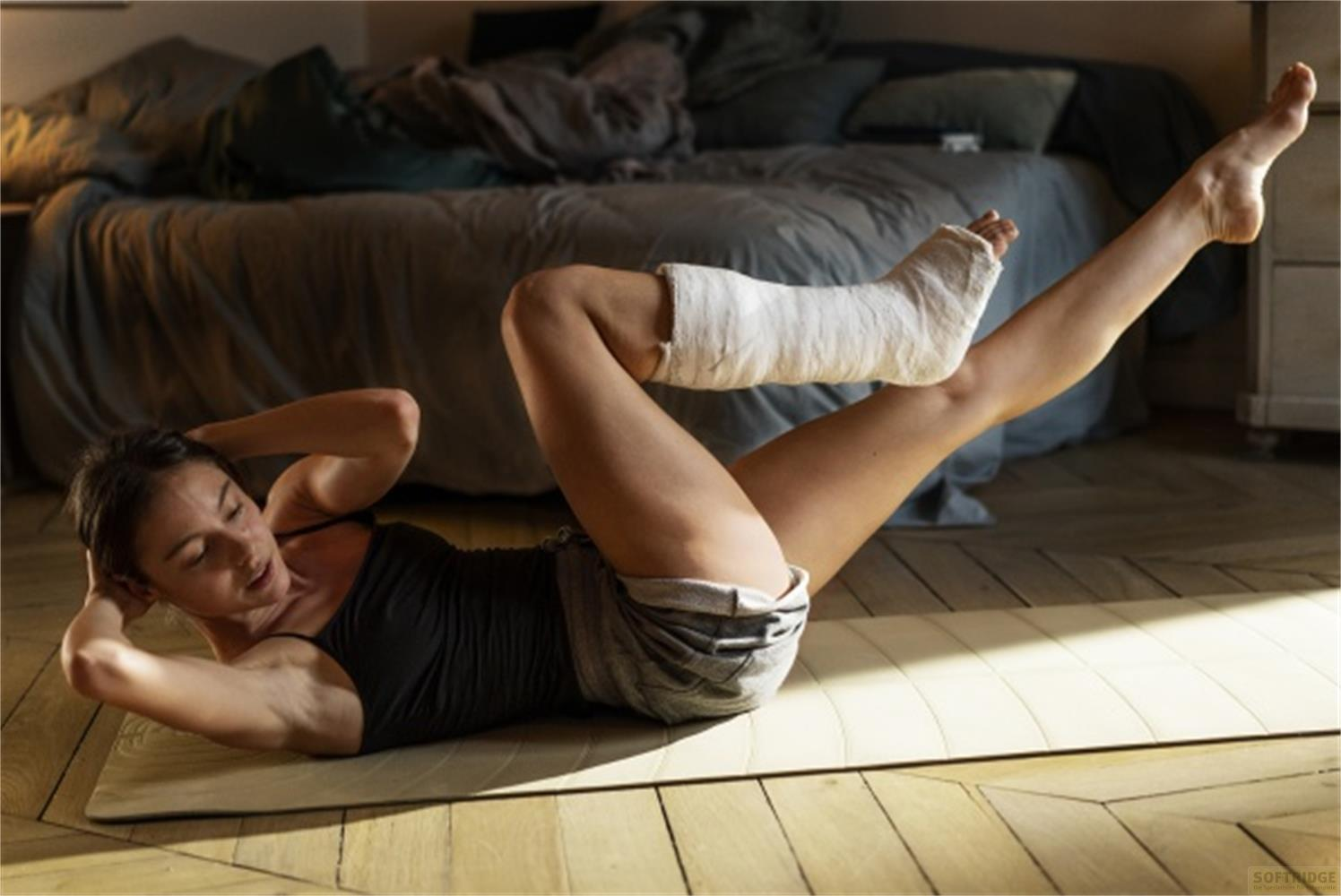 Donna con gamba ingessata fa crunch su un tappetino in una camera da letto.