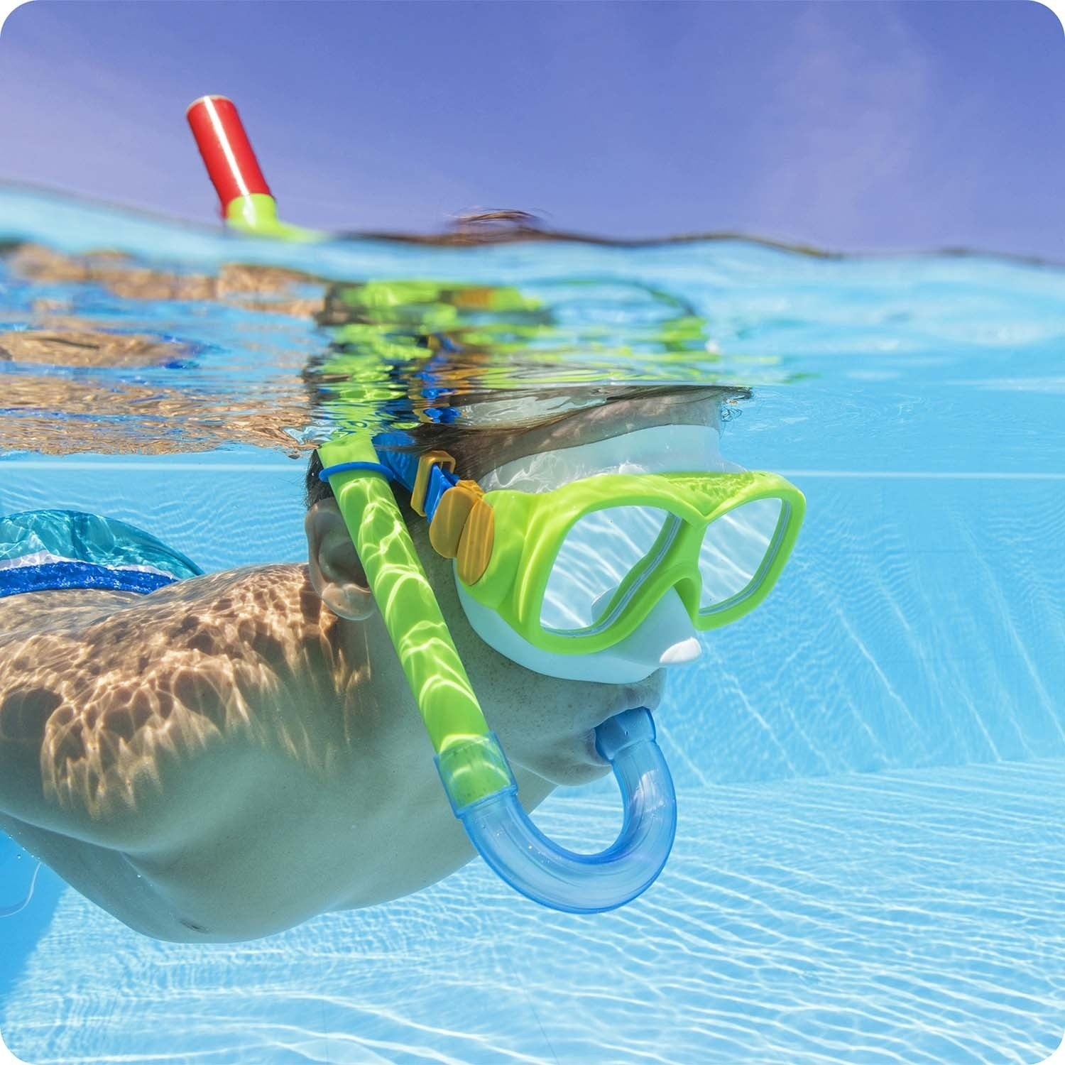 Persona con máscara de snorkel nada bajo el agua en piscina. Sol brillante.