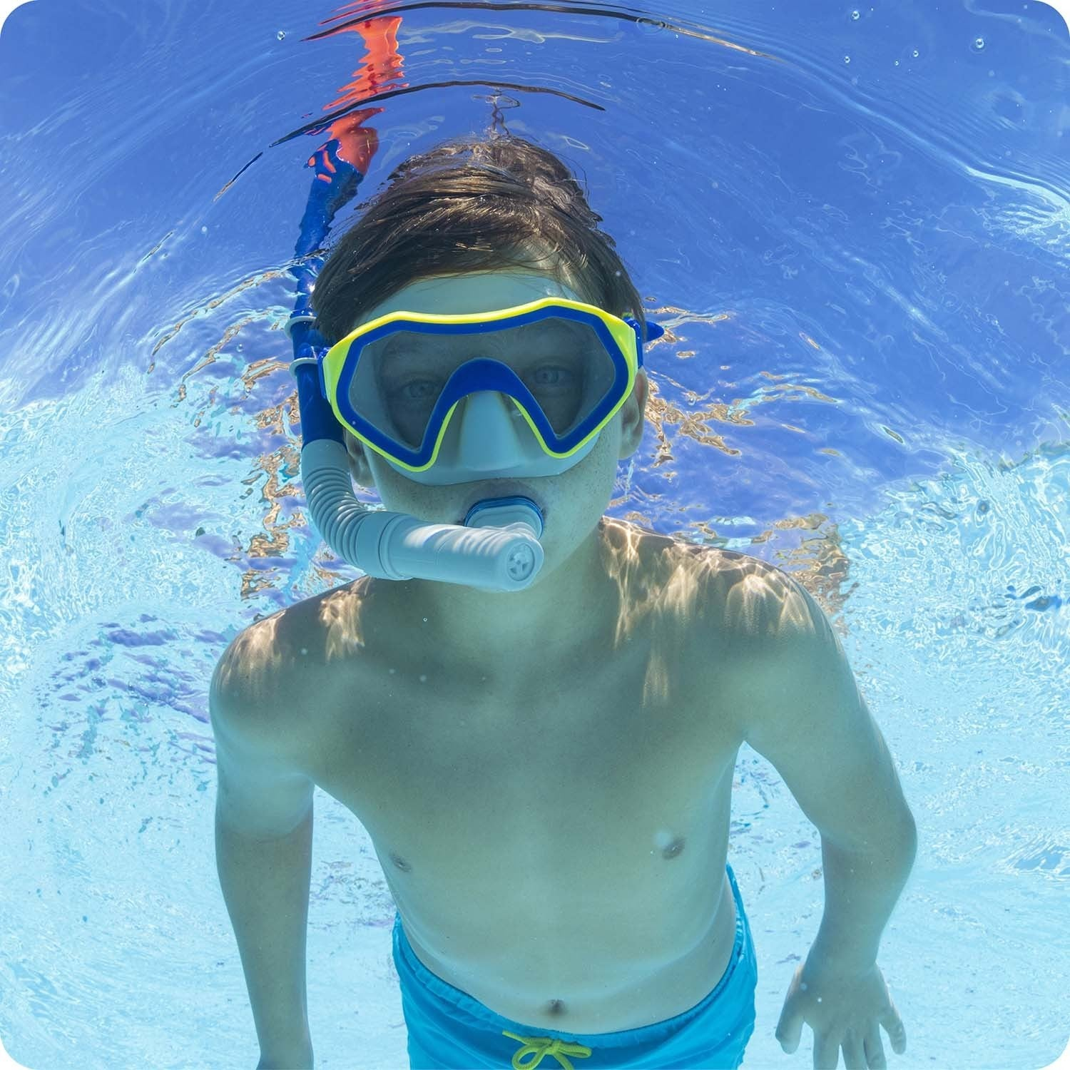 Niño con máscara de snorkel nada bajo el agua en una piscina.