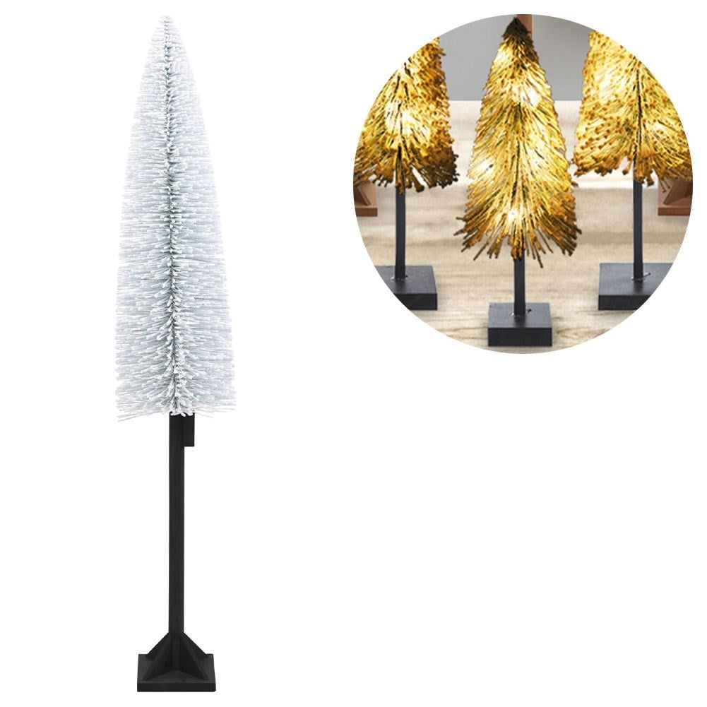 Un árbol blanco artificial a la izquierda, tres árboles dorados iluminados a la derecha.