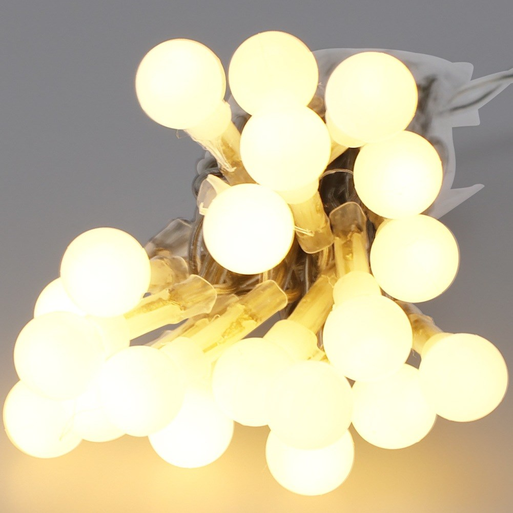 Un primer plano de muchas luces de hadas pequeñas, redondas y de color blanco cálido colgadas sobre un fondo gris.