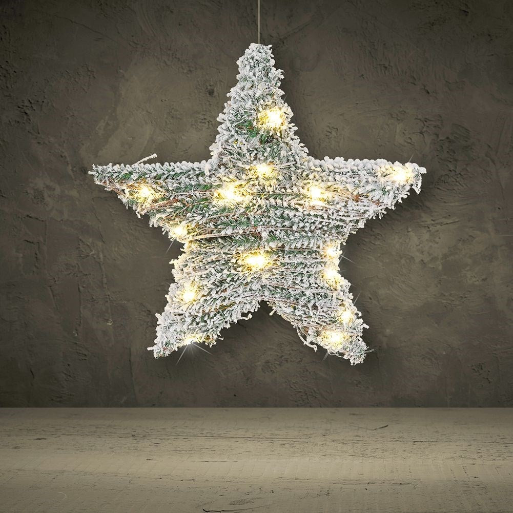 Una estrella de ramas de pino con nieve y luces cuelga frente a una pared.
