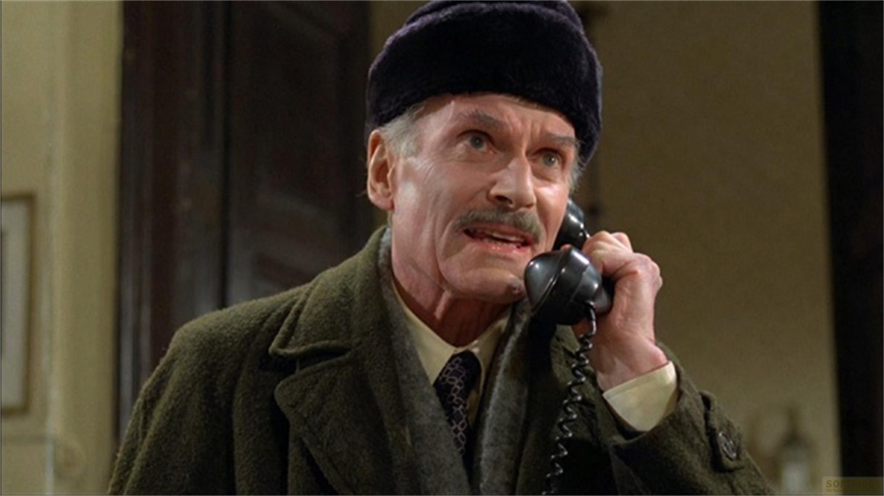 Un uomo anziano con i baffi indossa un cappello nero e parla al telefono.