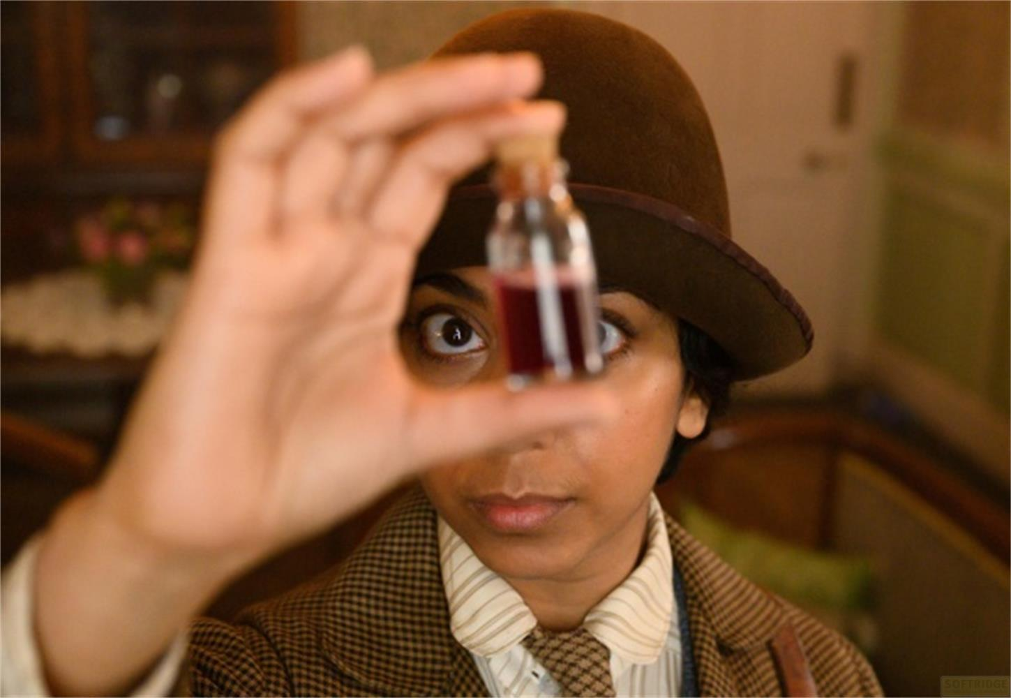 Una donna con il cappello tiene una piccola bottiglia di liquido rosso davanti al viso.