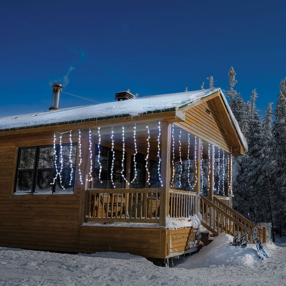 Porche de cabaña de madera con luces de carámbano blancas y nieve. Equipo de esquí cerca.