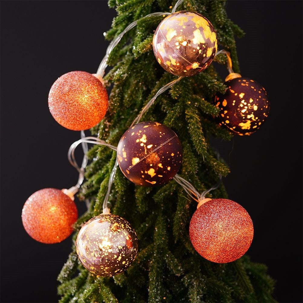 Bolas brillantes con purpurina y motas en una rama de árbol de Navidad.