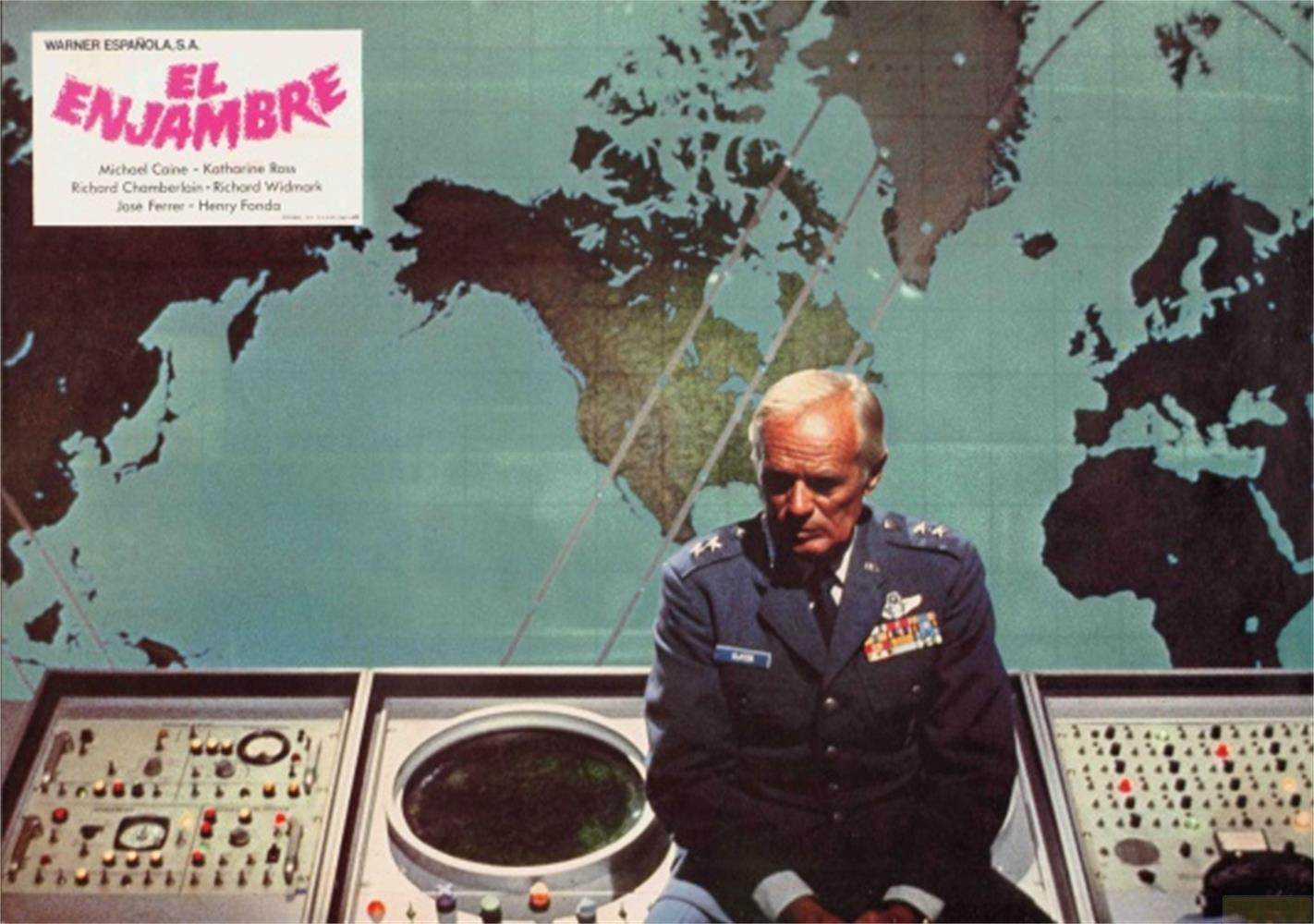 Uomo in uniforme seduto davanti a un mappamondo e pannelli di controllo.