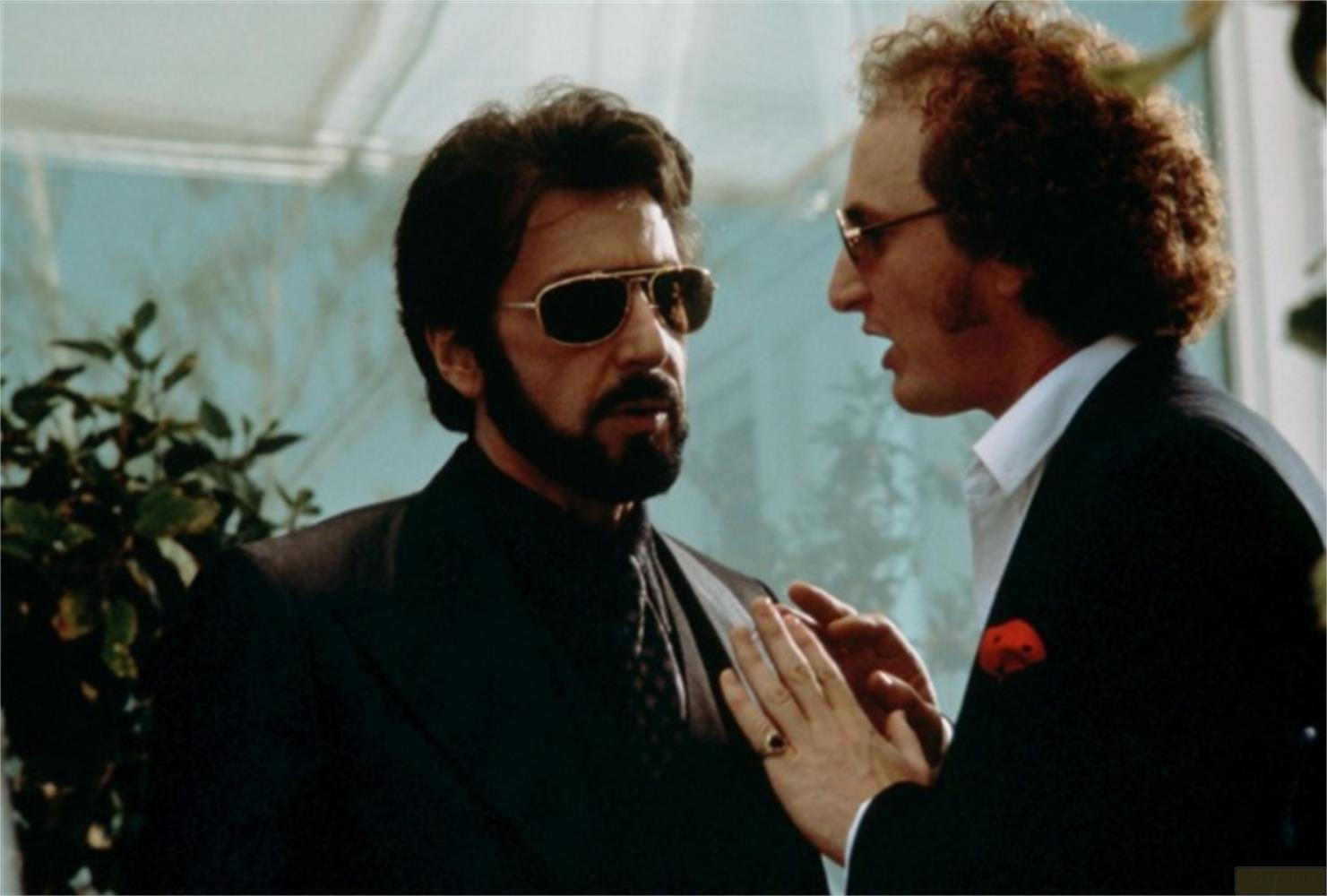Deux hommes en costume parlent. L'un porte des lunettes de soleil.