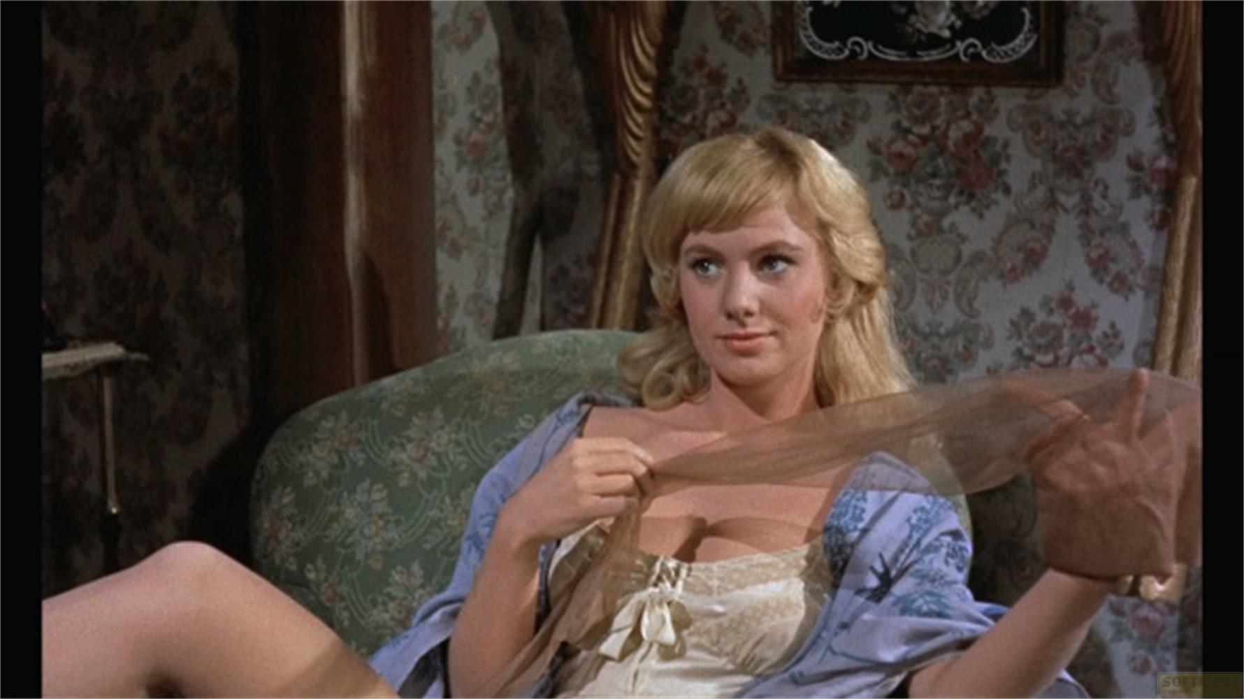 Una donna bionda seduta su un divano verde fantasia tiene in mano tessuto trasparente.