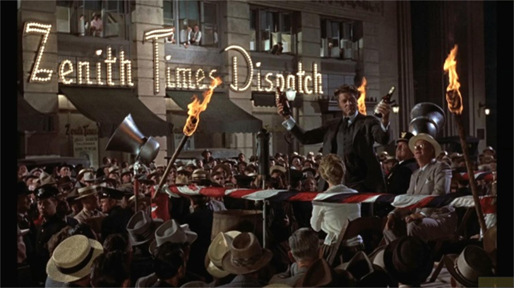 Un uomo tiene in alto una bottiglia davanti a una folla con torce e insegna Zenith Times.
