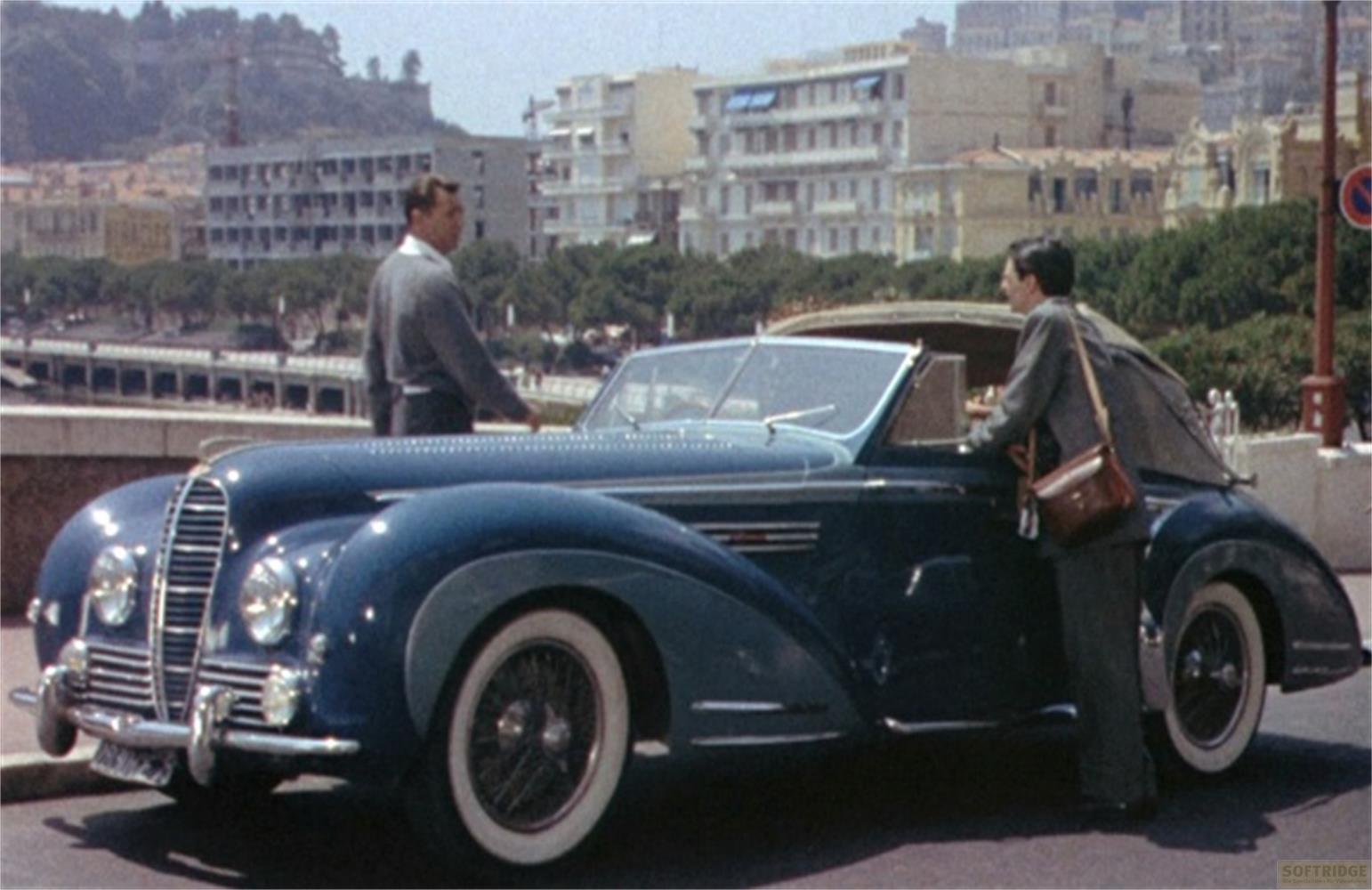 Due uomini accanto a un'auto d'epoca blu scuro cabriolet con pneumatici a fascia bianca.