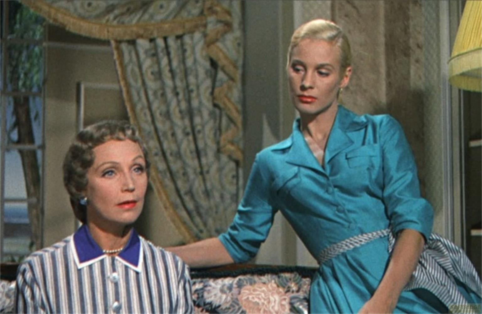 Due donne sedute su un divano. Una indossa un vestito blu, l'altra una camicia a righe.