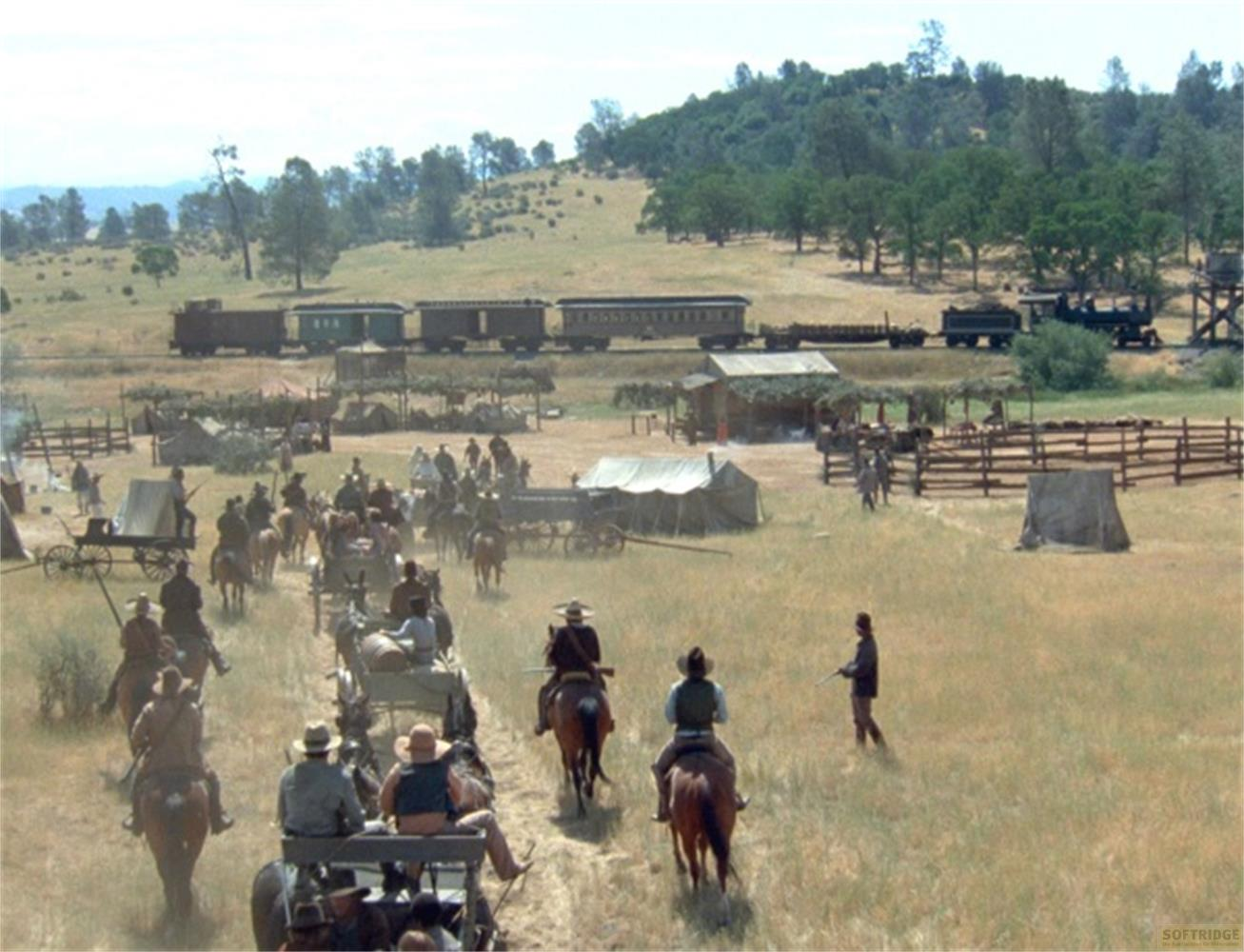Una scena western con persone a cavallo e carri vicino a un treno e tende.