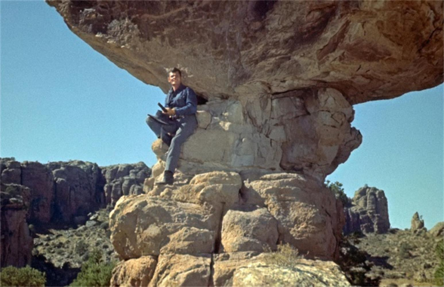 Un uomo seduto su una roccia sotto una sporgenza in un paesaggio roccioso.