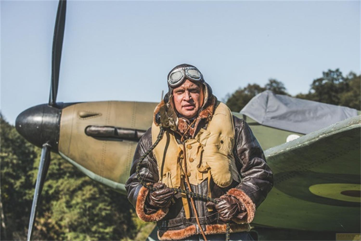 Un pilote en blouson de cuir et lunettes se tient à côté d'un avion à hélice.