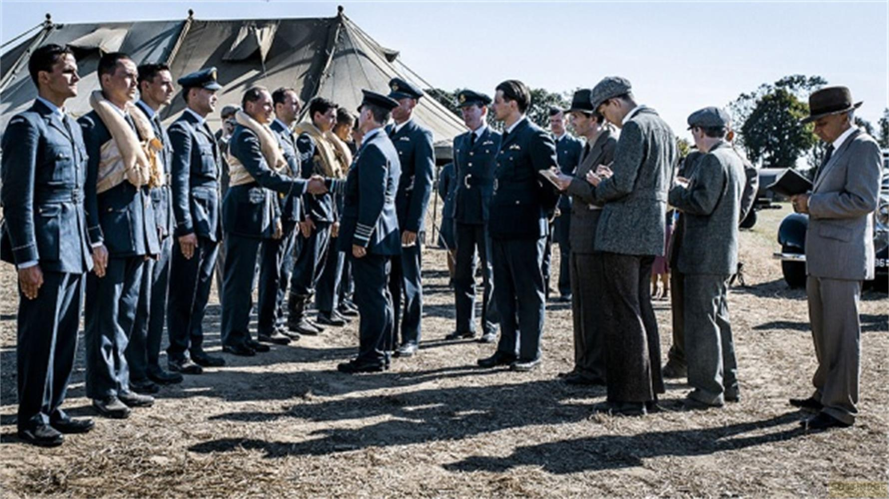 Des hommes en uniforme et civils se tiennent dehors devant une tente.