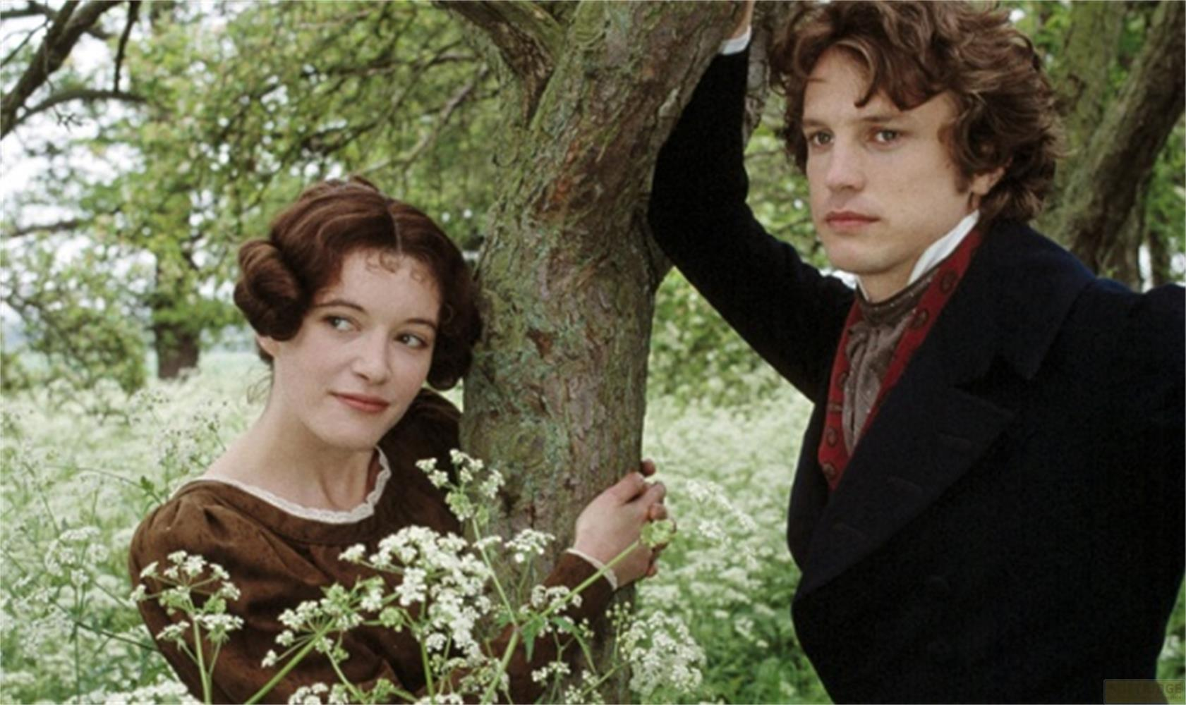 Un uomo e una donna in piedi all'aperto vicino a un albero. Piante fiorite bianche in primo piano.