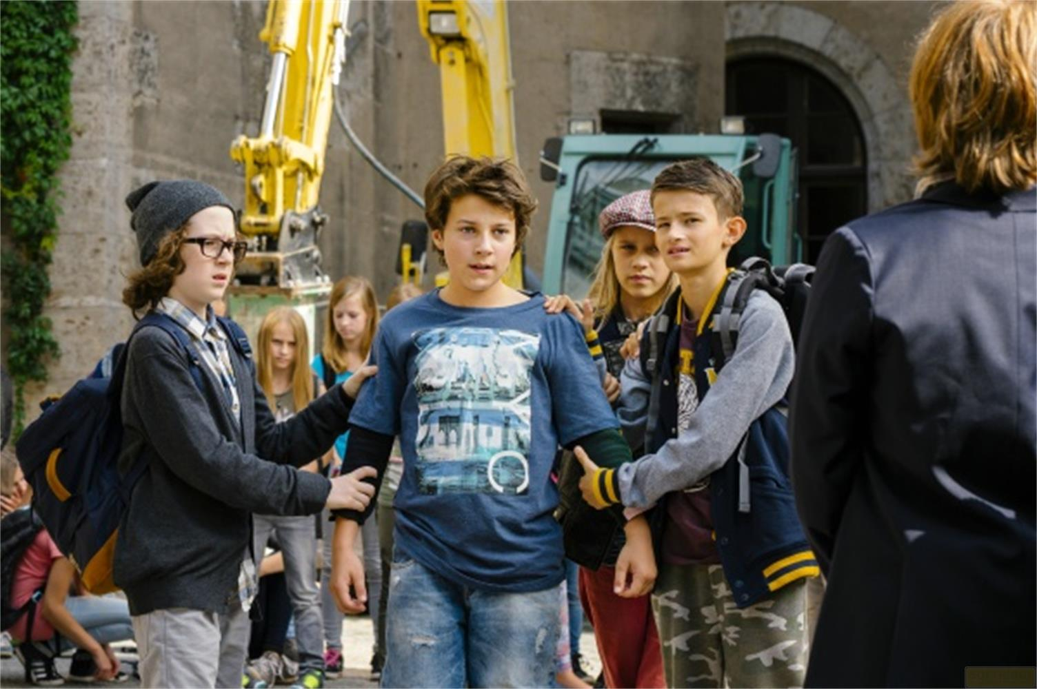 Kinder stehen vor einer Baustelle mit Baggern. Einer hält einen Rucksack.