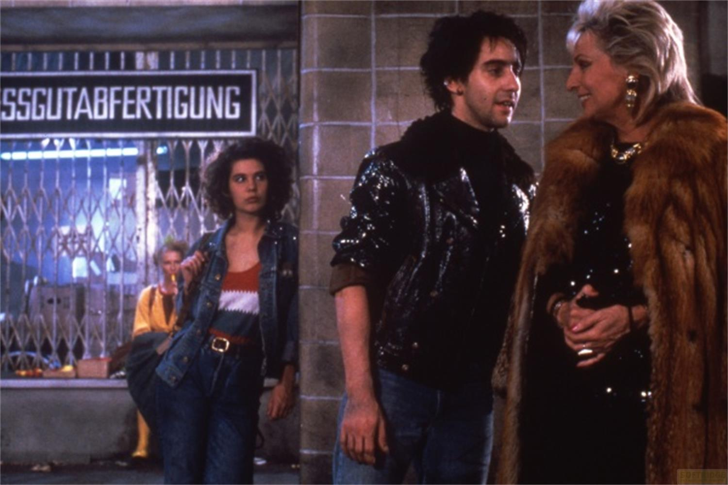 Tre persone davanti a un negozio. Donna in giacca di jeans, uomo in giacca glitterata, donna in pelliccia.