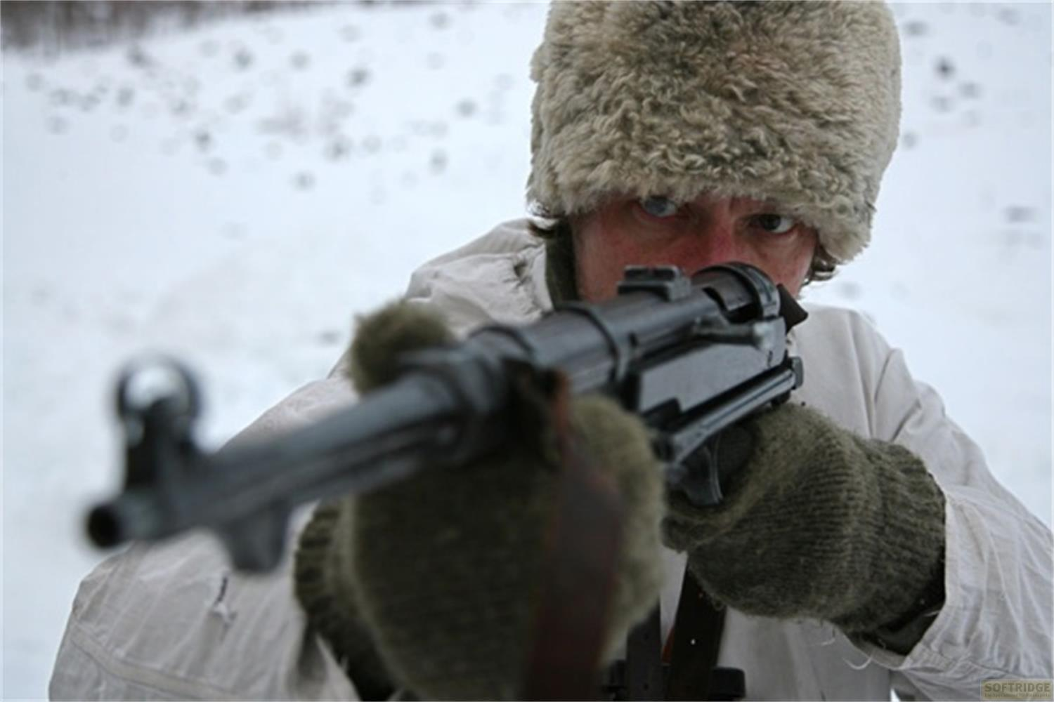 Uomo con pistola nella neve, cappello invernale, primo piano.