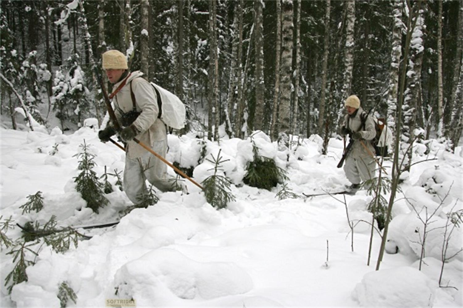 Due soldati in mimetica invernale bianca con fucili camminano nella neve alta in una foresta.