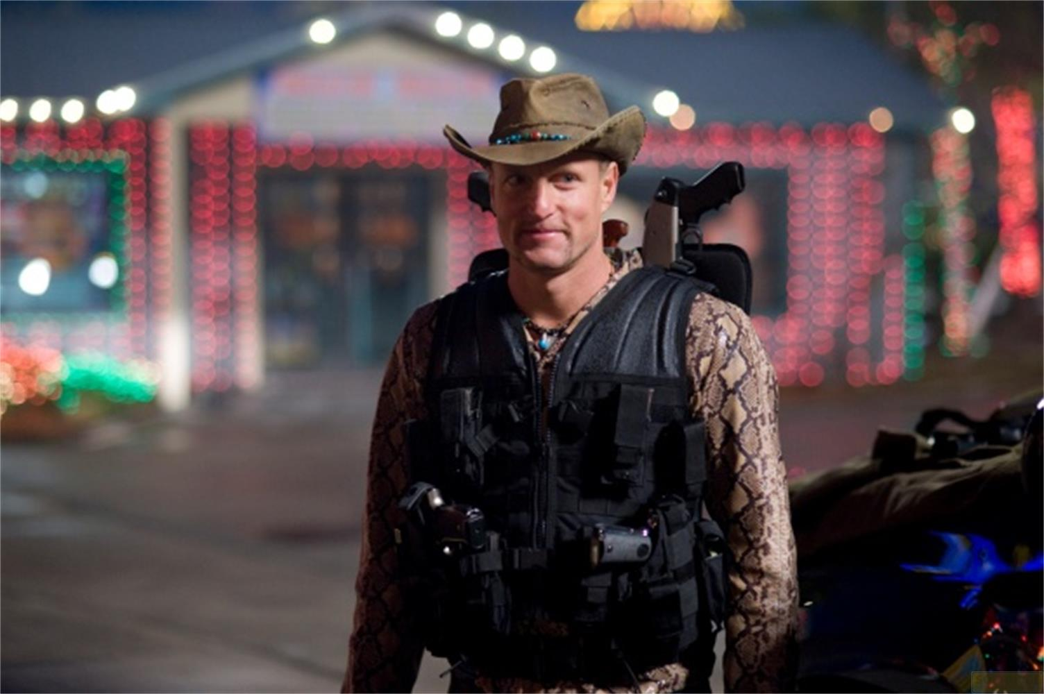 Un homme au chapeau de cowboy et à la chemise en peau de serpent porte un gilet tactique.
