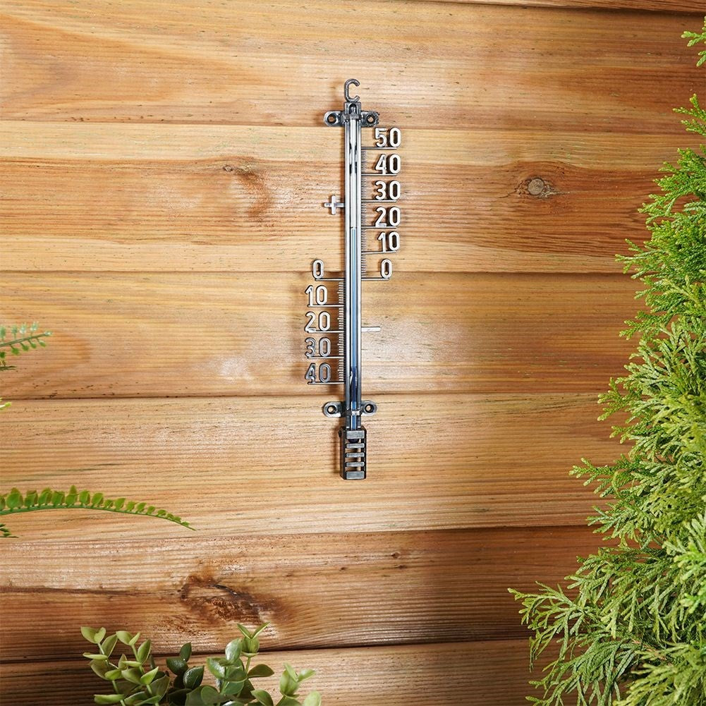 Un termómetro cuelga de una pared de madera, con plantas verdes al lado.