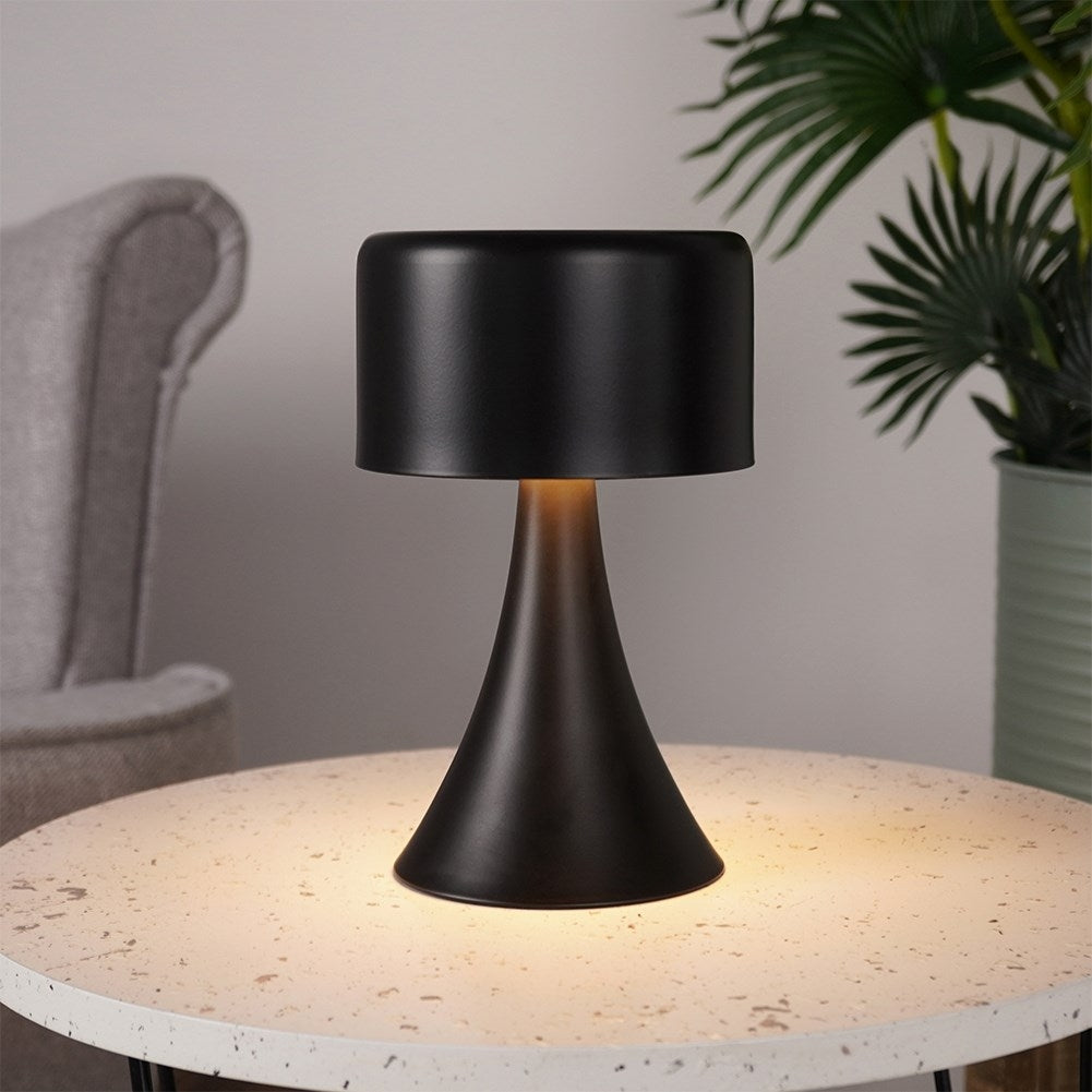Una lámpara de mesa negra con pantalla cilíndrica está sobre una mesa redonda.