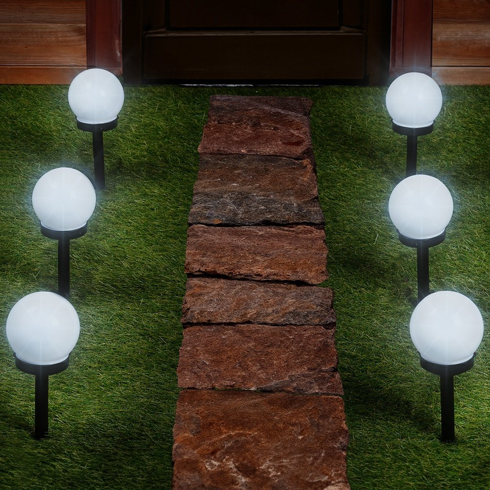 Un camino de losas de piedra atraviesa un césped con seis luces esféricas blancas.