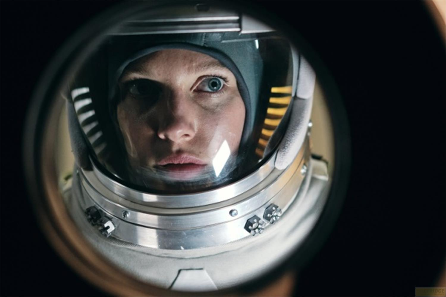 Una donna in tuta spaziale guarda attraverso la visiera di un casco. Primo piano.